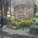 メキシコの観光ガイド岩﨑功がオルメカの人頭像の前で挨拶をしている