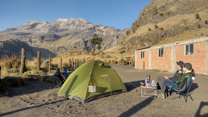Sano sama Izta base - メキシコのプライベートツアー | MCT 左に緑色のテント、右に二人の男女が座って奥の山を眺めている