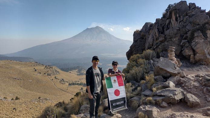 高山をバックに男女二人が日本とメキシコの国旗を掲げている
